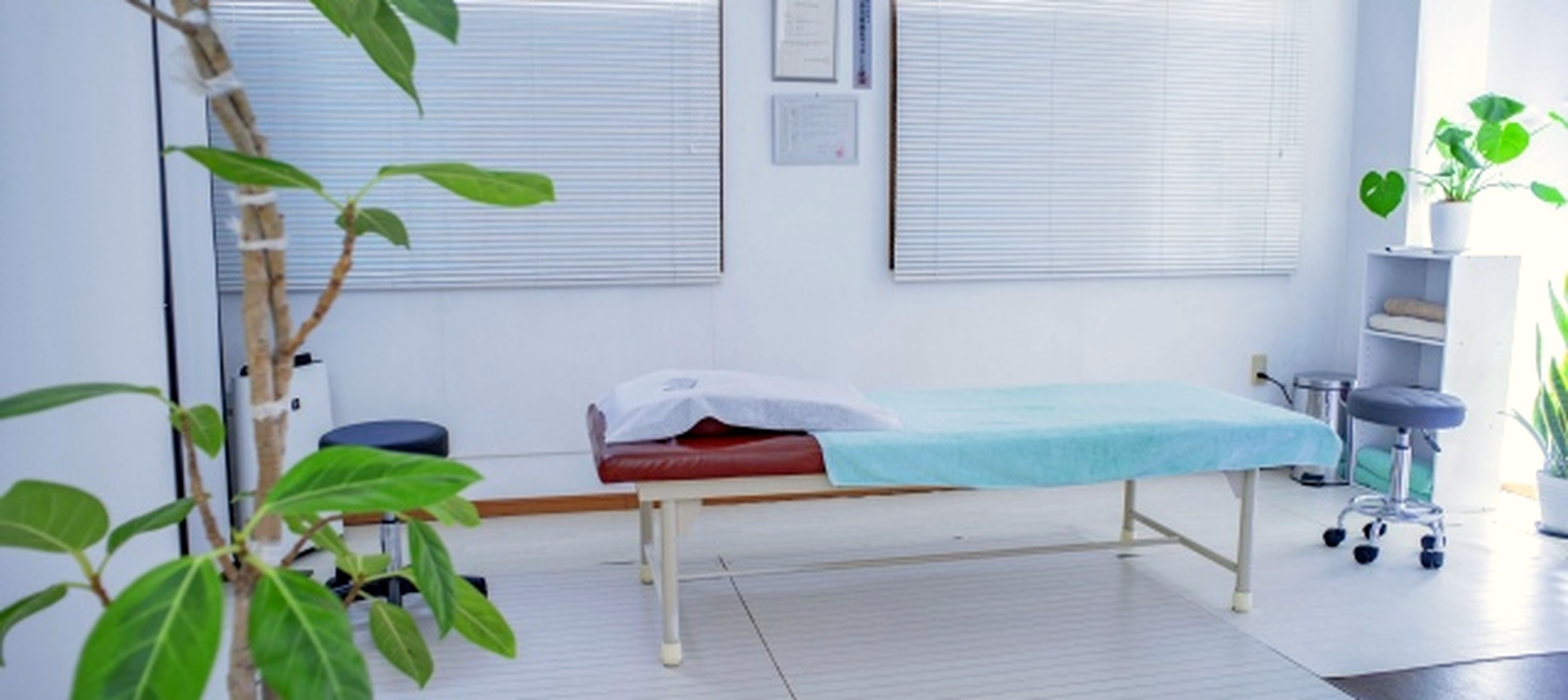 快晴鍼灸院の施術室ワイド。ブラインド越しの自然光と整然とした設備が並ぶ落ち着いた内観。